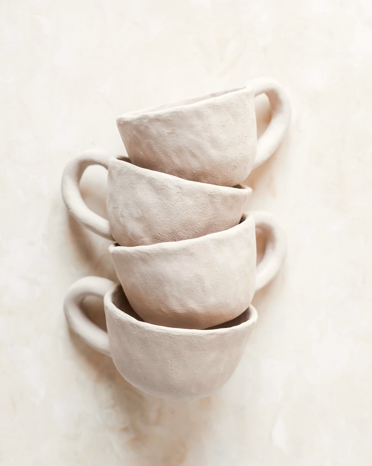 Four hand-built ceramic cups stacked on a pale surface