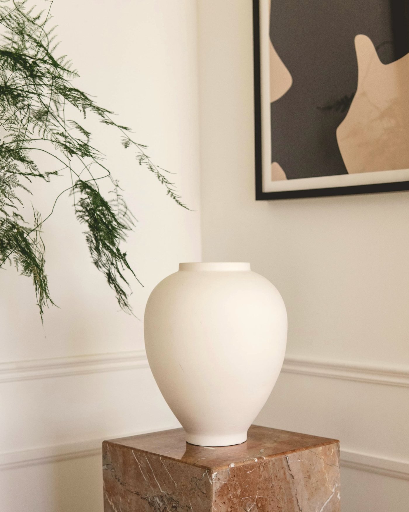 Chalk-white stoneware Plinth Vase on a travertine plinth beside a framed artwork